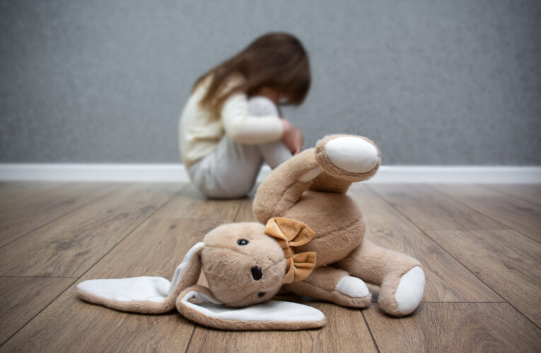 A stuffed bunny on the floor, a scared child sitting behind it. Child abuse. Bullying in the family.