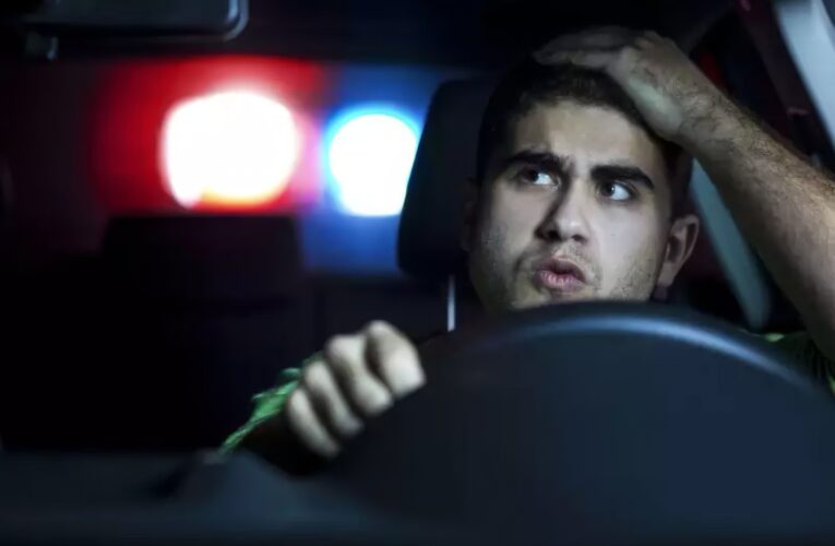 Driver Pulled Over by Police at Night with Flashing Lights in Rearview Mirror